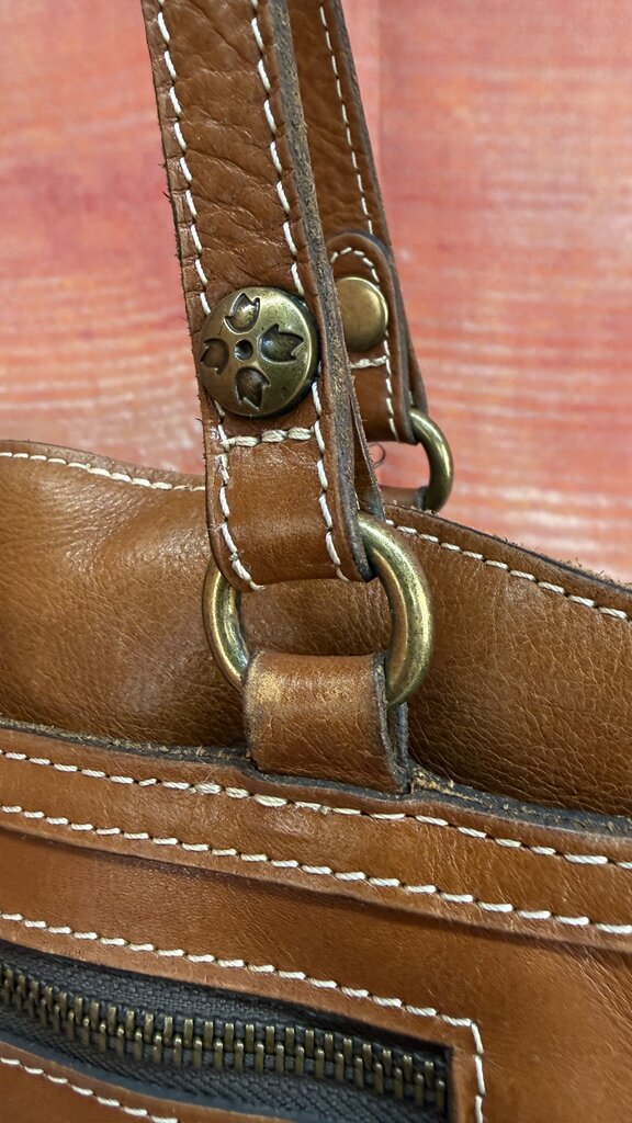 Close-up of a brown leather bag with gold hardware on a red-brown background